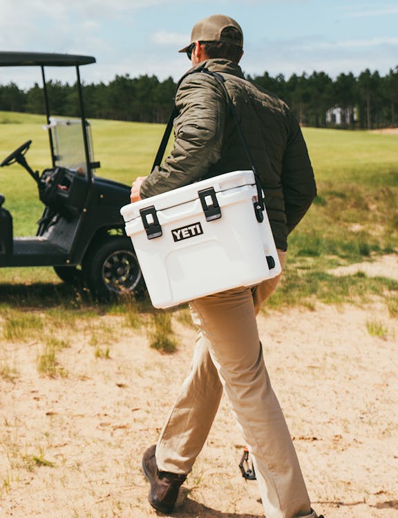 man walking with roadie 15 in white over his shoulder on golf course.